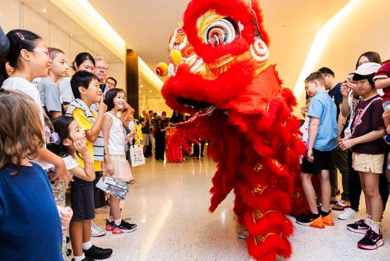 Children and adults watching a display of a red puppet dragon.