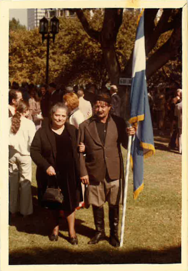 Aged photo of a man and a woman with linked arms and the man holding the flag of Crete.
