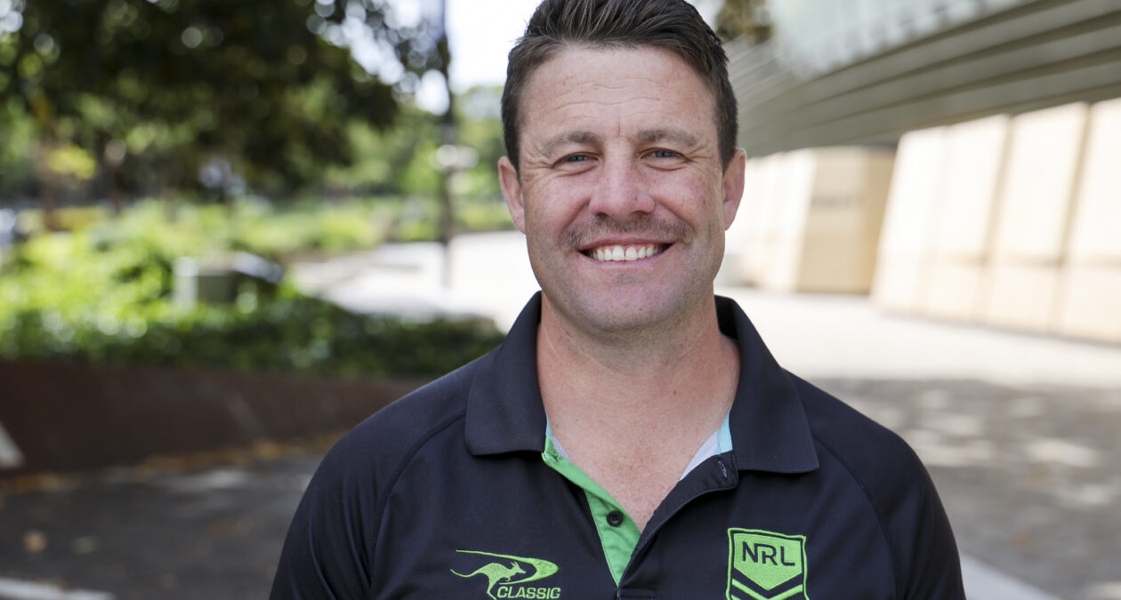 Man in polo shirt with NRL logo smiling at the camera.