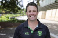 Man in polo shirt with NRL logo smiling at the camera.