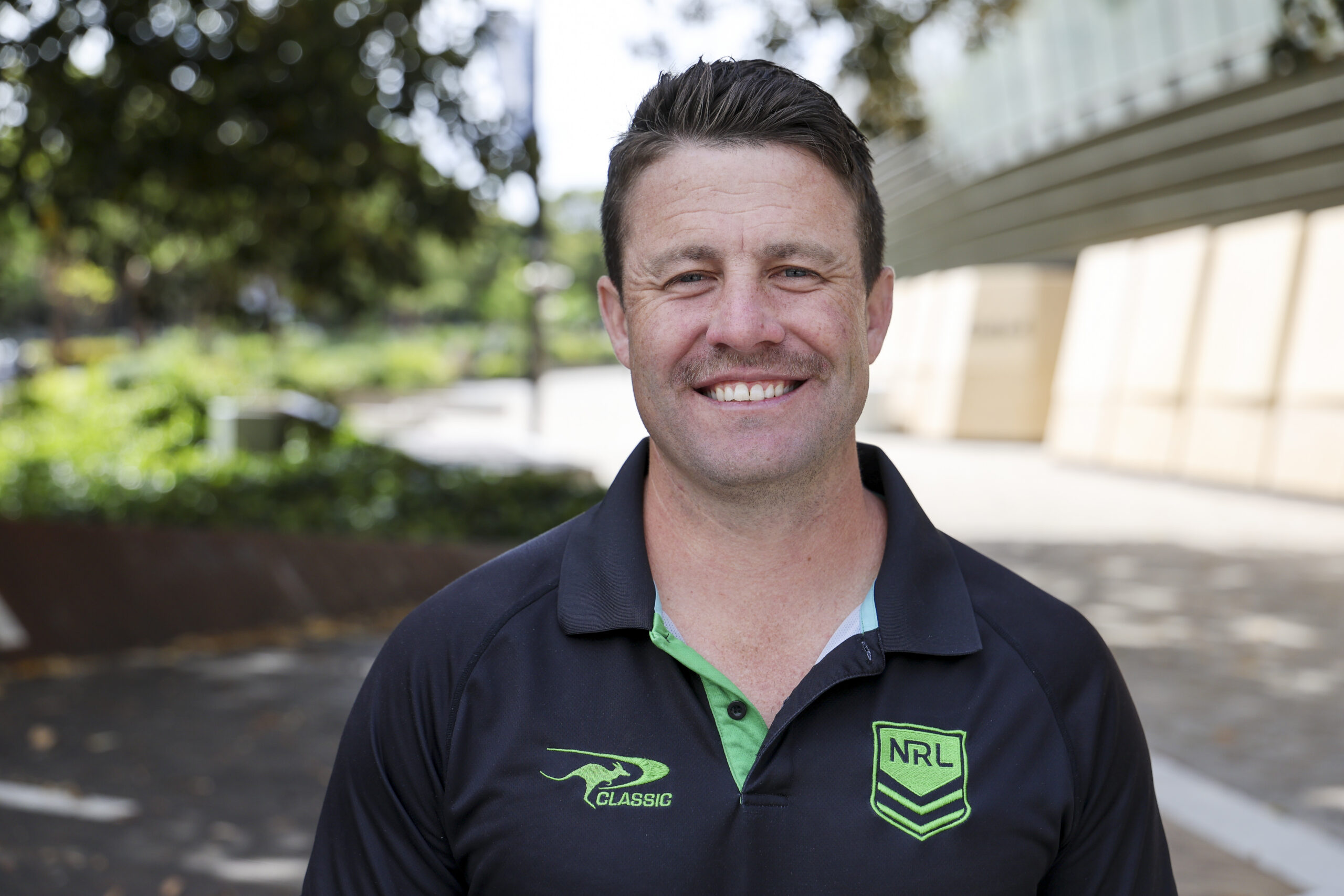 Man in polo shirt with NRL logo smiling at the camera.