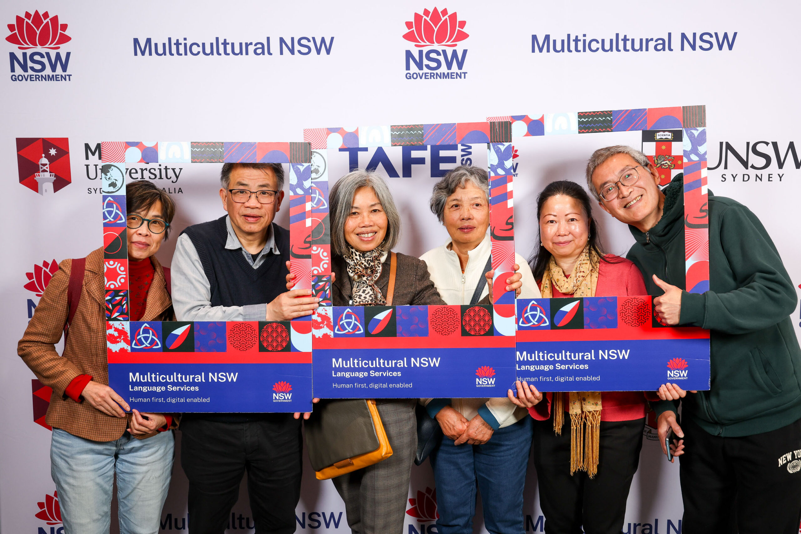 Six people holding and looking through selfie frames in front of a media wall.
