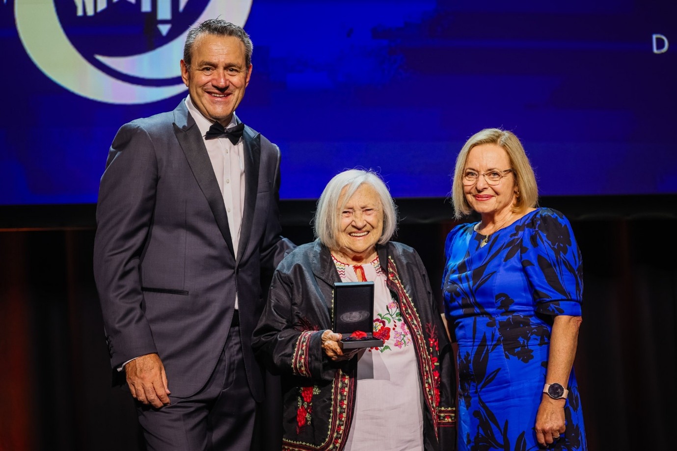 A woman holding a medal with a NSW Minister and another woman alongside.