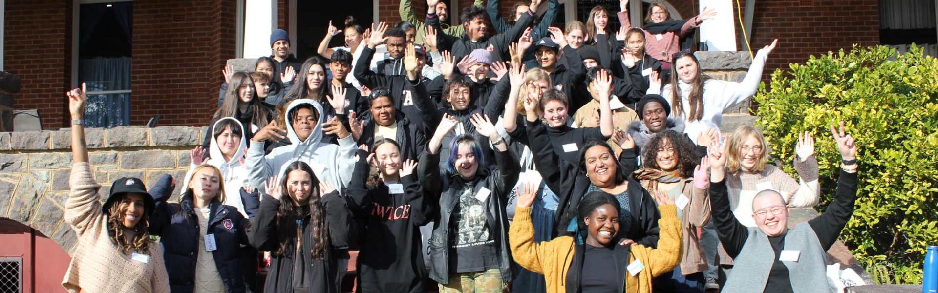 A group of young people standing outside in the sunshine in the steps of a house.