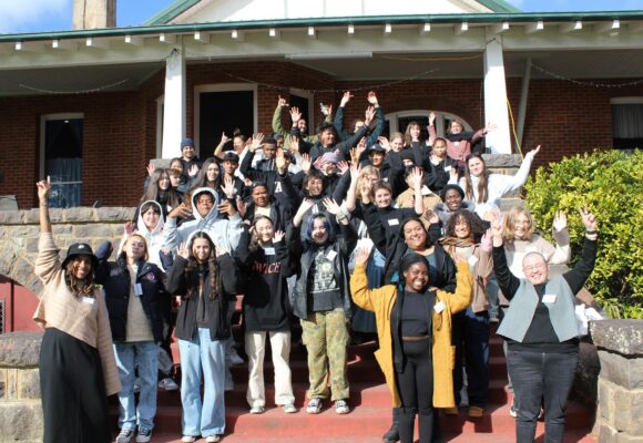 A group of young people standing outside in the sunshine in the steps of a house.