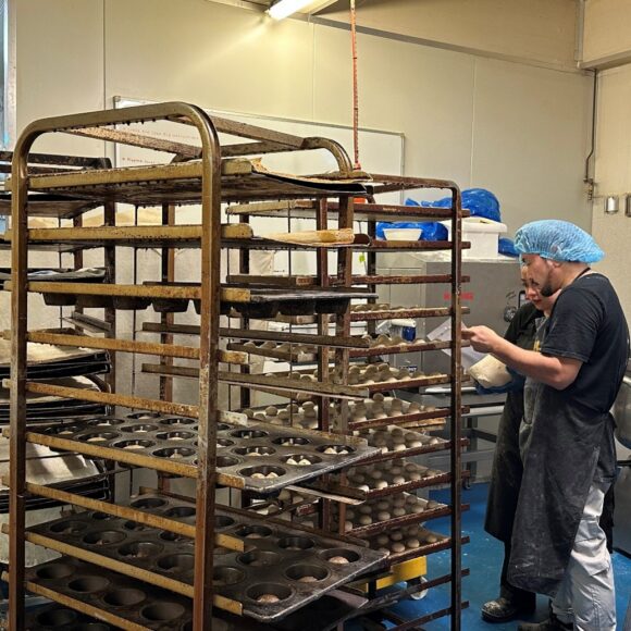 Two people wearing hairnets adding rolled dough to baking trolleys.