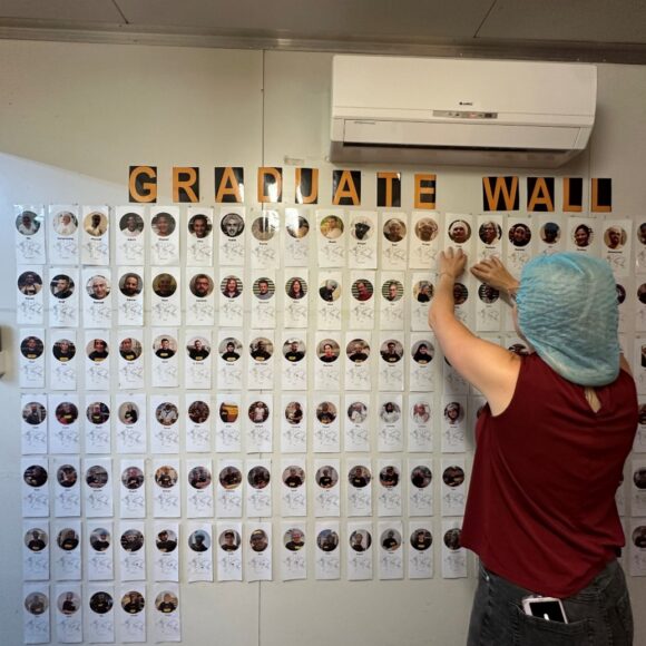 Person in a hairnet adding a card to a image wall called 'graduate wall'.