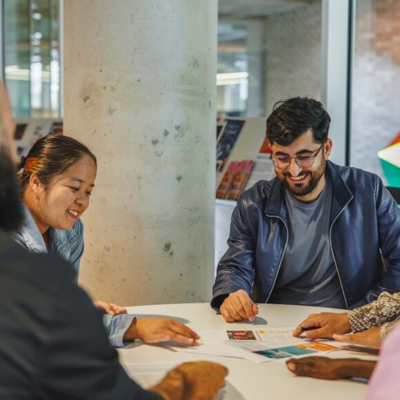 Four people in an inside meeting sitting at a table looking at paperwork.