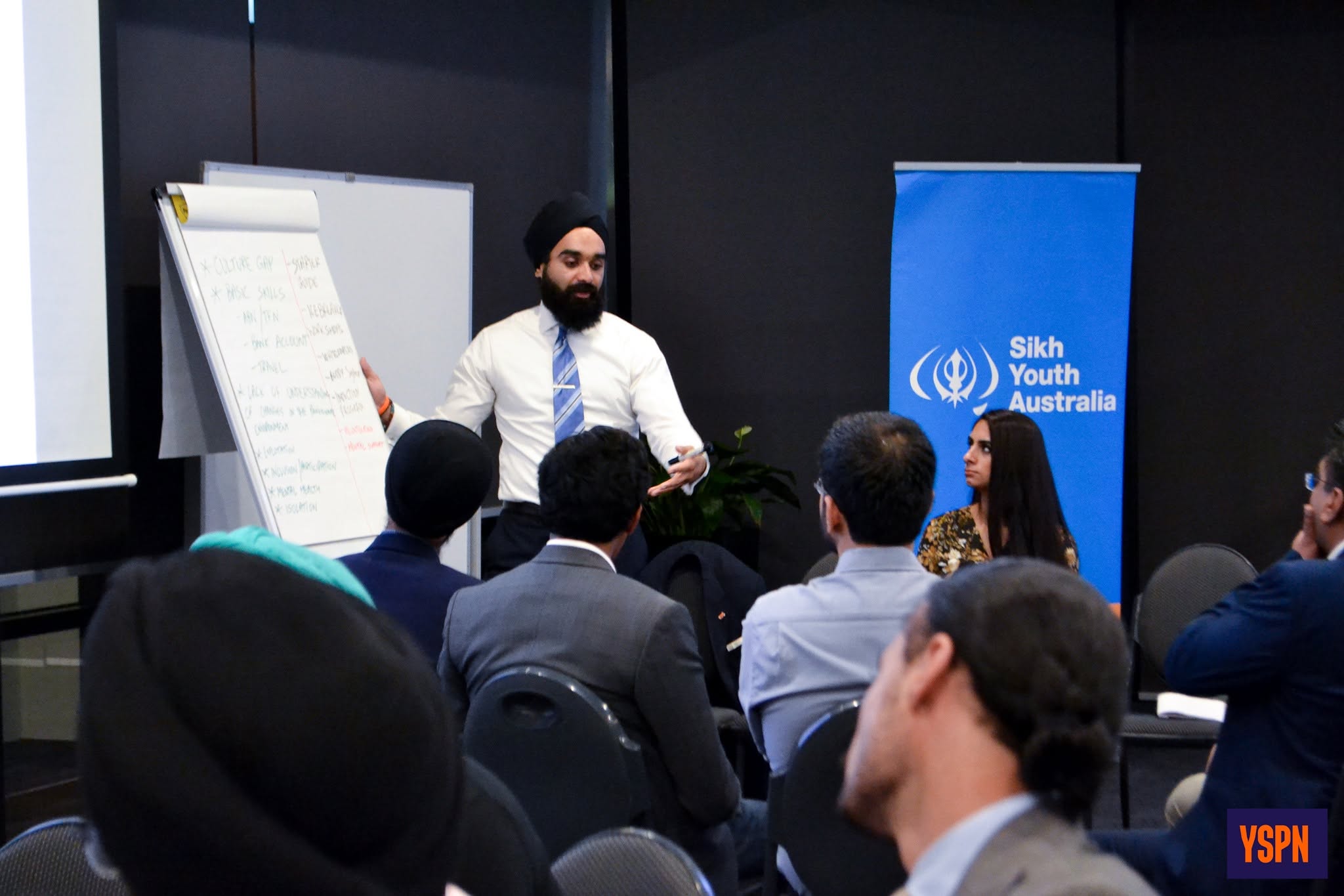 A man standing in front of a presentation pad talking to a group of people.