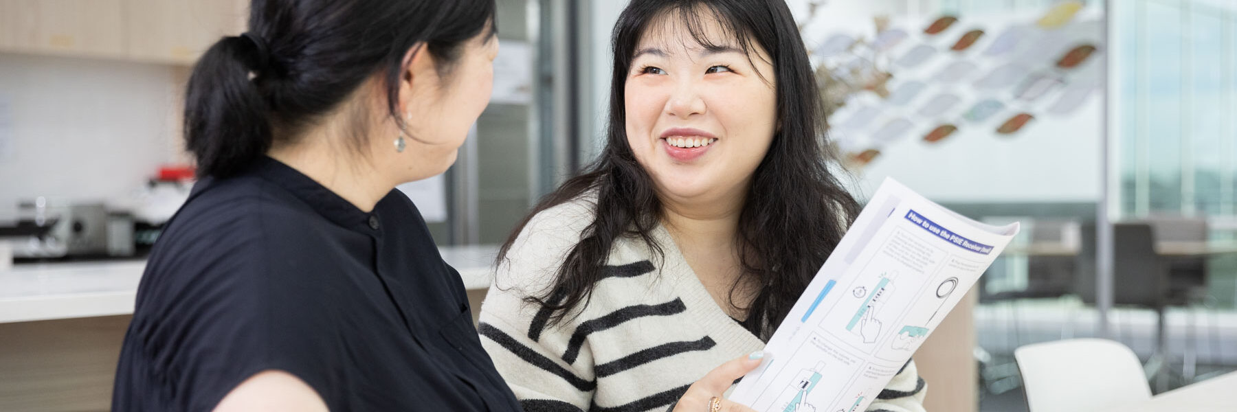 Two women sitting at a bench inside looking at some brochures.