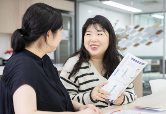 Two women sitting at a bench inside looking at some brochures.